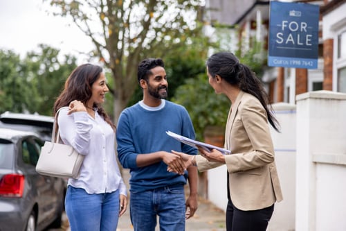 Couple discutant avec une agente immobilière devant une maison à vendre pour évaluer la cession d’un bien locatif rentable