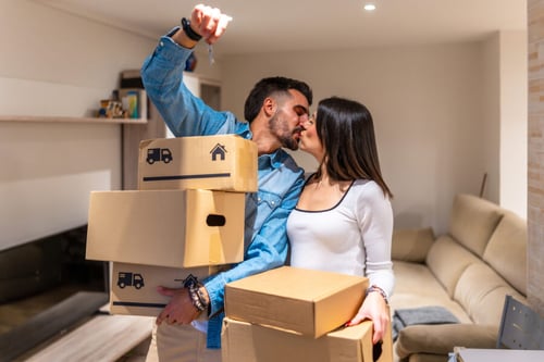 Couple en train d’emménager dans un nouveau logement avec des cartons de déménagement illustrant le processus d’achat immobilier et la transition entre deux biens. L’homme porte une boîte marquée d’un logo de maison tandis que la femme observe, symbolisant les étapes avant un investissement dans l’immobilier. Cette scène représente les défis financiers liés à un prêt relais, solution temporaire pour acheter un nouveau bien avant la vente de l’ancien. Idéal pour un article sur les risques et avantages du crédit relais dans le cadre d’un projet immobilier et d’un financement par prêt bancaire. Déménagement, achat maison, prêt relais, crédit immobilier, transition logement, risques financiers, investissement immobilier.
