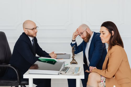 Trois personnes en réunion tendue autour d’un bureau discutant des responsabilités liées au loyer après un divorce entre loca