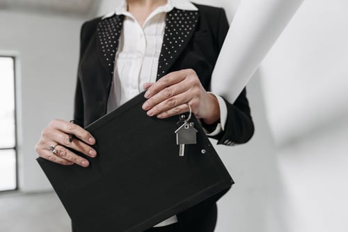 Femme en tailleur tenant une clé et un dossier représentant un état des lieux de sortie avec un propriétaire ou agent immobil