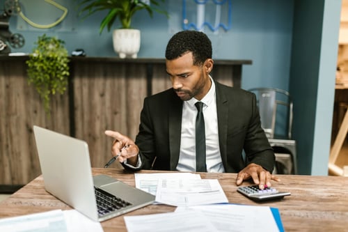 Homme en costume analysant des documents et utilisant une calculatrice pour gérer la facture électronique dans un bureau prof