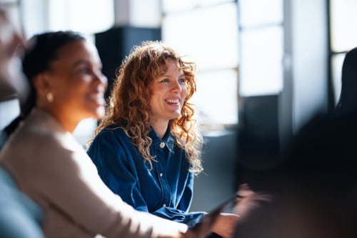 Femme souriante avec des cheveux bouclés en réunion professionnelle dans un bureau lumineux, discutant des démarches pour faire intervenir un garant en cas de loyers impayés. Plusieurs personnes assises autour d’une table de travail, échangent des conseils juridiques et pratiques pour sécuriser le recouvrement des loyers. Ambiance collaborative et rassurante pour aborder les solutions en cas d’impayés de loyer et l’intervention efficace du garant locatif. Idéal pour illustrer un article sur la gestion des garanties locatives et les recours en cas de difficultés financières du locataire.