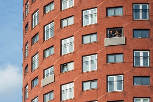 Façade d’un immeuble en briques rouges avec plusieurs balcons où des locataires profitent de leur logement sous un ciel dégag