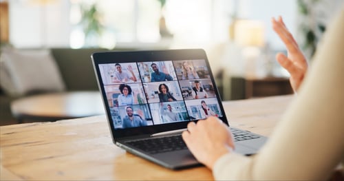 Une personne participe à une assemblée générale de copropriété à distance via une visioconférence sur son ordinateur portable. L’écran montre plusieurs participants en grille sur une plateforme de réunion en ligne, chacun dans son propre environnement. La scène se déroule dans un cadre cosy et lumineux, probablement à domicile, illustrant une solution pratique pour assister à une AG de copropriété sans se déplacer. Les gestes de la main suggèrent une interaction active, mettant en avant les avantages du télétravail et des outils numériques pour les réunions à distance. Idéal pour les copropriétaires cherchant des alternatives pour voter et échanger efficacement depuis chez eux.