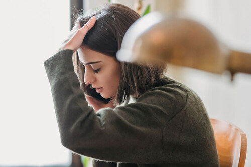Jeune femme stressée au téléphone cherchant désespérément un logement à louer dans un bureau éclairé