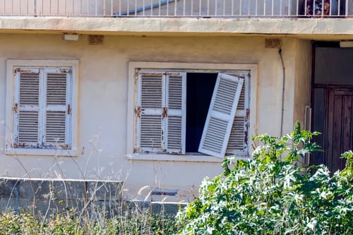 Fenêtres anciennes aux volets en bois délabrés d'une maison abandonnée ou squattée illustrant les défis des propriétaires face au squat en France. Cette image représente les conséquences matérielles du squat dans le cadre du durcissement de la loi Kasbarian prévue en 2027 pour renforcer la protection des propriétaires. Les volets abîmés et la végétation envahissante soulignent l'importance des mesures législatives pour lutter contre l'occupation illicite des logements et faciliter les procédures d'expulsion des squatteurs. Contexte immobilier et sécurisation des biens face à la nouvelle réglementation antisquat.