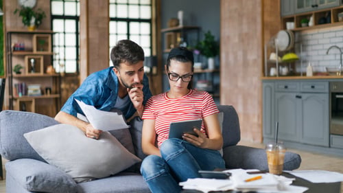 Couple étudiant examinant des documents et une tablette pour comprendre les charges locatives dans leur salon lumineux