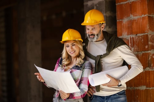 Deux professionnels en tenue de chantier examinent des plans de VEFA devant un bâtiment en construction
