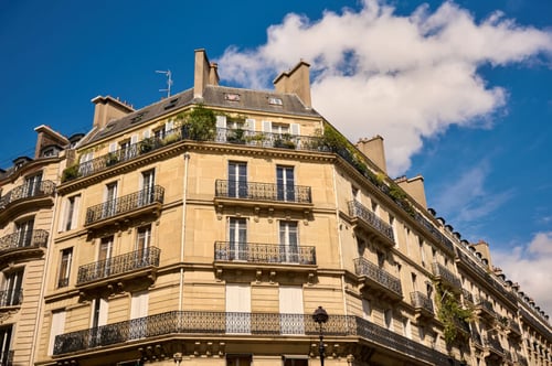 Immeuble haussmannien typique de Paris avec balcons en fer forgé et façades en pierre beige sous un ciel bleu partiellement nuageux. Cet édifice parisien, caractérisé par ses fenêtres alignées et ses détails architecturaux élégants, illustre le cadre de vie des étudiants étrangers en France. Dans le contexte des tensions au Moyen-Orient, cette image symbolise les défis rencontrés par ces étudiants, notamment les difficultés financières liées aux impayés et aux contraintes économiques exacerbées par les crises géopolitiques. Parfaite pour évoquer les réalités des logements étudiants à Paris et les enjeux socio-économiques actuels.