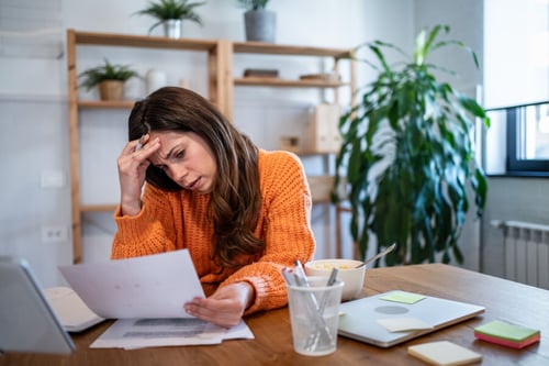 Femme stressée lisant un avis d’expulsion locative à son bureau à domicile. Elle se tient la tête, visiblement préoccupée, devant des documents officiels et un ordinateur portable. La scène se déroule dans un intérieur lumineux avec des étagères en bois, des plantes vertes et des fournitures de bureau, illustrant l’impact concret des expulsions locatives record en 2023. Cette image reflète la détresse des locataires confrontés à des procédures d’expulsion et s’inscrit dans le contexte d’une hausse historique des expulsions en France, abordé dans l’article sur les difficultés du logement et les solutions pour les locataires en situation précaire.