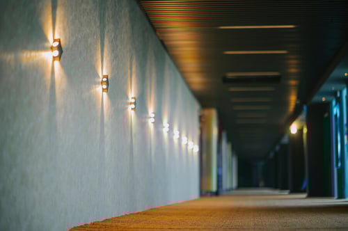 Décoration intérieure avec éclairage chaleureux pour améliorer l'ambiance acoustique d'une pièce sans travaux. Cette image montre une série de suspensions lumineuses design descendant le long d'un mur texturé aux tons clairs, créant une atmosphère apaisante et tamisée. Les luminaires diffusent une lumière douce, idéale pour réduire la perception des bruits indésirables en ajoutant des éléments esthétiques qui absorbent indirectement les sons. Parfait pour illustrer des solutions simples et élégantes d’isolation phonique naturelle, comme l’utilisation de tissus, de tapis épais au premier plan et d’objets décoratifs pour atténuer les échos dans une pièce. Idéal pour un intérieur moderne cherchant à optimiser le confort acoustique sans recourir à des rénovations lourdes.