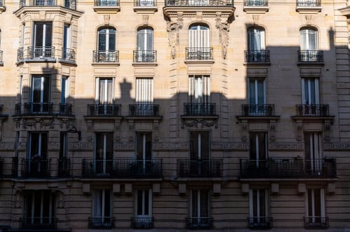 Façade d'un immeuble haussmannien typique avec balcons en fer forgé et fenêtres à la française, illustrant le charme de l'ancien avec ses moulures ornées et ses pierres de taille claires. Cet exemple d'architecture parisienne traditionnelle du XIXe siècle met en valeur les détails élégants et le cachet historique, éléments souvent recherchés par les locataires en quête de caractères authentiques dans leur logement.