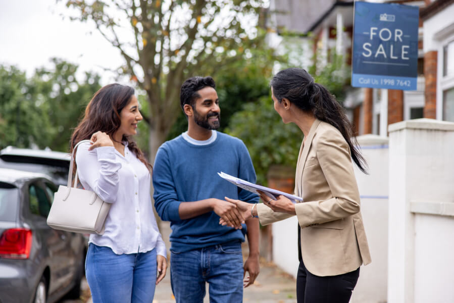 Couple discutant avec une agente immobilière devant une maison à vendre pour évaluer la cession d’un bien locatif rentable