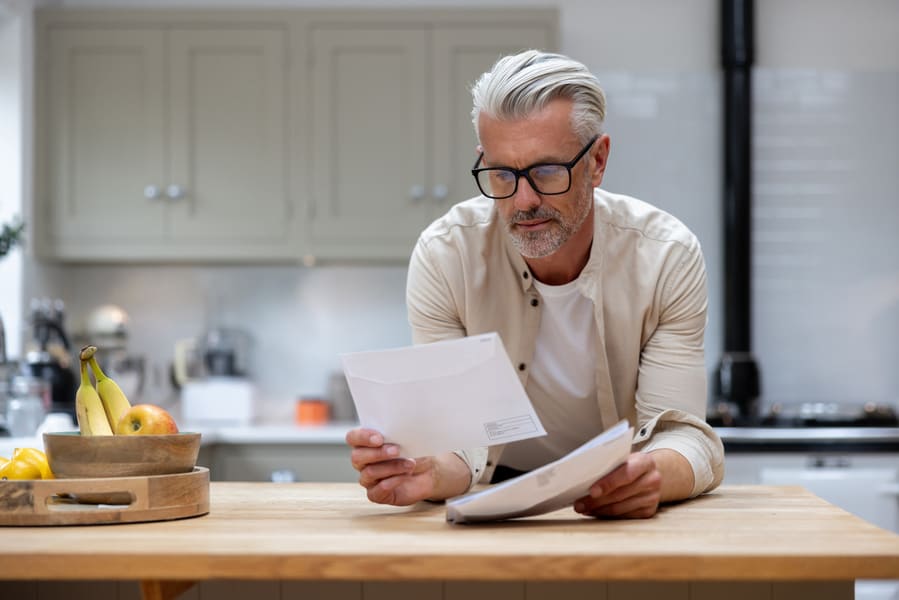 Propriétaire lisant des documents dans sa cuisine, réfléchissant à la gestion du départ d’un colocataire.