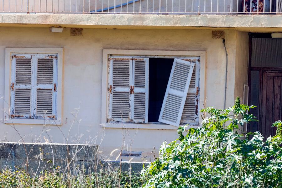 Fenêtres anciennes aux volets en bois délabrés d'une maison abandonnée ou squattée illustrant les défis des propriétaires face au squat en France. Cette image représente les conséquences matérielles du squat dans le cadre du durcissement de la loi Kasbarian prévue en 2027 pour renforcer la protection des propriétaires. Les volets abîmés et la végétation envahissante soulignent l'importance des mesures législatives pour lutter contre l'occupation illicite des logements et faciliter les procédures d'expulsion des squatteurs. Contexte immobilier et sécurisation des biens face à la nouvelle réglementation antisquat.