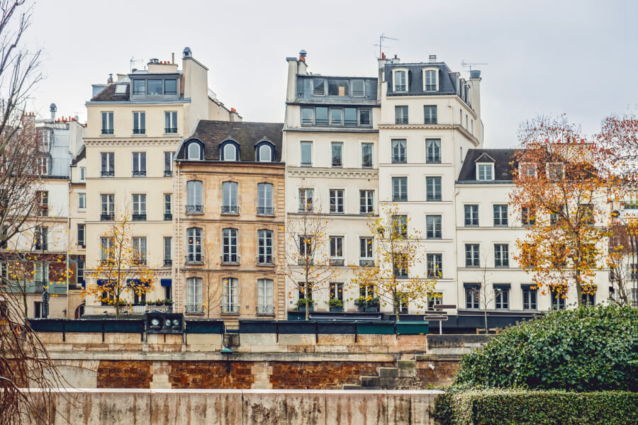 Découvrez un exemple typique d’immeuble parisien ancien le long des berges de Seine, illustrant les défis de la vente d’un appartement avec un Diagnostic de Performance Énergétique (DPE) G. Cette photo montre plusieurs bâtiments haussmanniens et post-haussmanniens aux façades classiques, caractérisés par leurs fenêtres alignées, leurs balcons en fer forgé et leurs toits en zinc avec lucarnes. Ces constructions, souvent mal isolées, sont fréquemment concernées par les nouvelles réglementations thermiques, rendant leur vente plus complexe. Dans le cadre d’un article sur la vente d’un bien immobilier avec un DPE G, cette image met en avant l’importance des travaux de rénovation énergétique pour améliorer la performance thermique et valoriser le bien sur le marché. Un contexte essentiel pour les propriétaires souhaitant vendre un appartement énergivore dans une grande ville comme Paris.