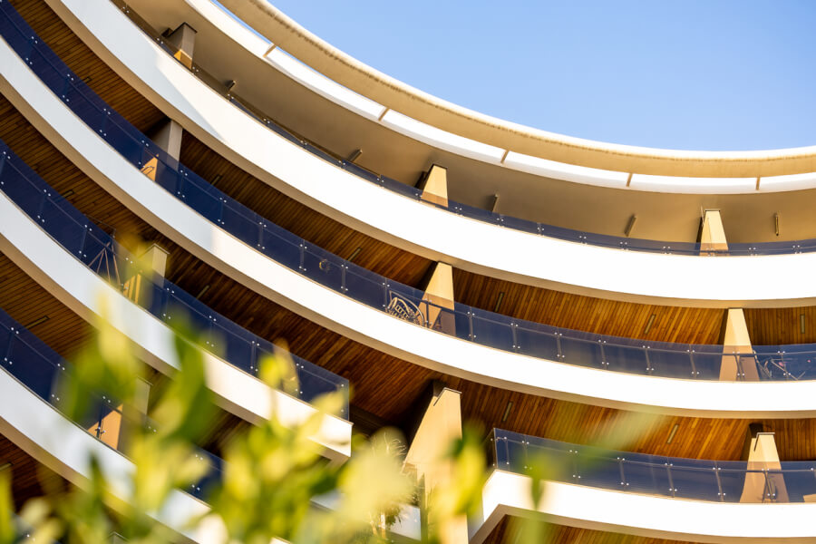 Balcons arrondis en étages d'un immeuble moderne avec garde-corps en verre teinté bleu, illustrant une résidence contemporaine susceptible d'accueillir des locataires ou garants résidant à l'étranger, sous un ciel dégagé.