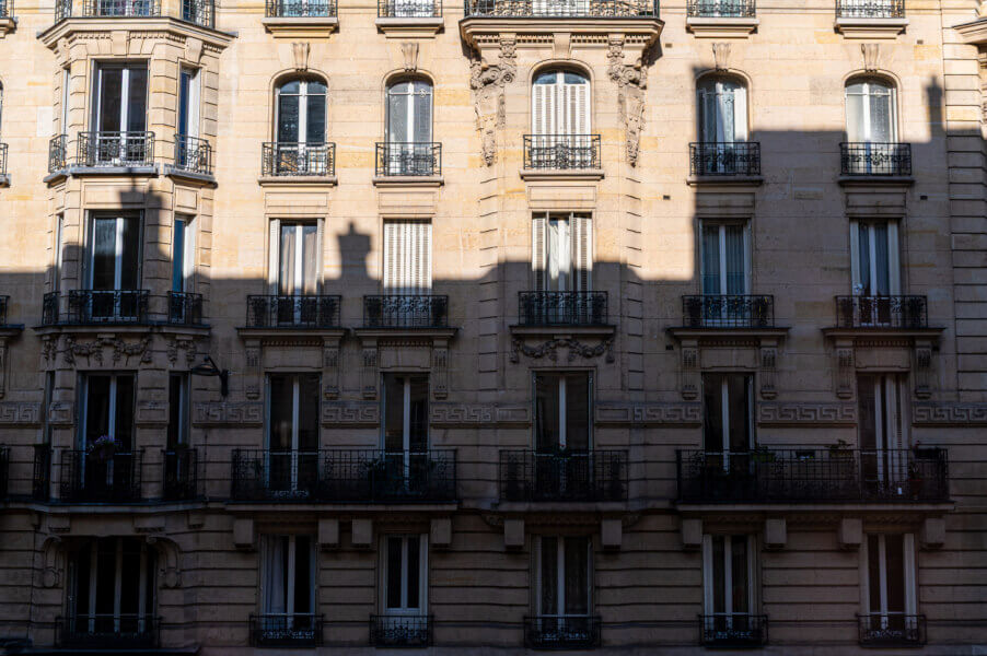 Façade d'un immeuble haussmannien typique avec balcons en fer forgé et fenêtres à la française, illustrant le charme de l'ancien avec ses moulures ornées et ses pierres de taille claires. Cet exemple d'architecture parisienne traditionnelle du XIXe siècle met en valeur les détails élégants et le cachet historique, éléments souvent recherchés par les locataires en quête de caractères authentiques dans leur logement.